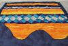 A colorful quilt with wavy orange, blue, yellow, and diamond-patterned strips, and a scalloped edge at the bottom. The quilt lies flat on a light surface.