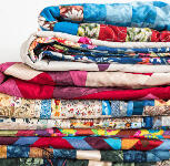 A stack of colorful, patterned quilts neatly folded on a white surface, with various vibrant fabric designs visible.