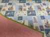 A handmade quilt featuring pastel blue, yellow, and white patchwork squares with playful cartoon animals like giraffes, elephants, and zebras. The quilt’s back is solid pink with a green border.