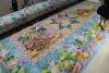 A long-arm quilting machine is stitching a colorful patchwork quilt with star patterns in a wooden room