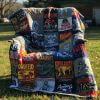 A quilt draped over a chair outdoors, made from various colorful rock band t-shirts featuring band names, logos, and album art. The background includes grass, trees, and a blurry house.