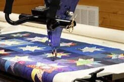 A long-arm quilting machine is stitching a colorful patchwork quilt with star patterns in a wooden room