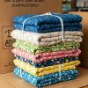 A neatly stacked pile of colorful, folded quilts tied with white strings, featuring various floral and patterned designs, set in front of large cardboard boxes. Quilting by mail.