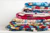 A stack of colorful, patterned quilts neatly folded on a white surface, with various vibrant fabric designs visible.