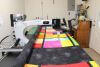 A quilting machine is stitching a colorful patchwork quilt with bright squares and rectangles on a large frame in a well-lit room.