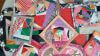 A collection of colorful, handmade quilted fabric coasters and mats in various shapes and sizes, featuring patchwork patterns with vibrant fabrics, displayed in an overlapping arrangement.