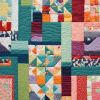 A colorful patchwork quilt featuring various geometric patterns and shapes in vibrant shades of blue, green, orange, red, pink, and purple, with visible stitching throughout.