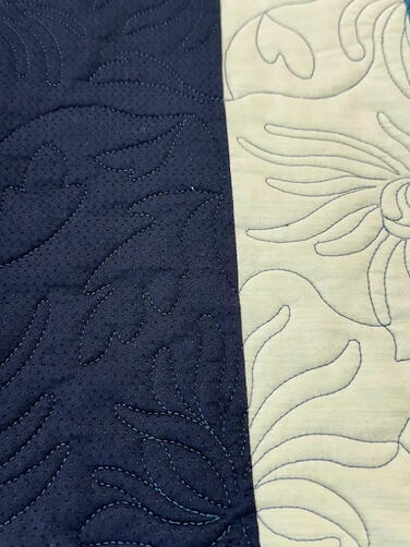A close-up of a quilt with vertical strips of patterned and solid fabrics in blue, teal, and cream tones, featuring intricate quilted stitching in swirling and floral designs.